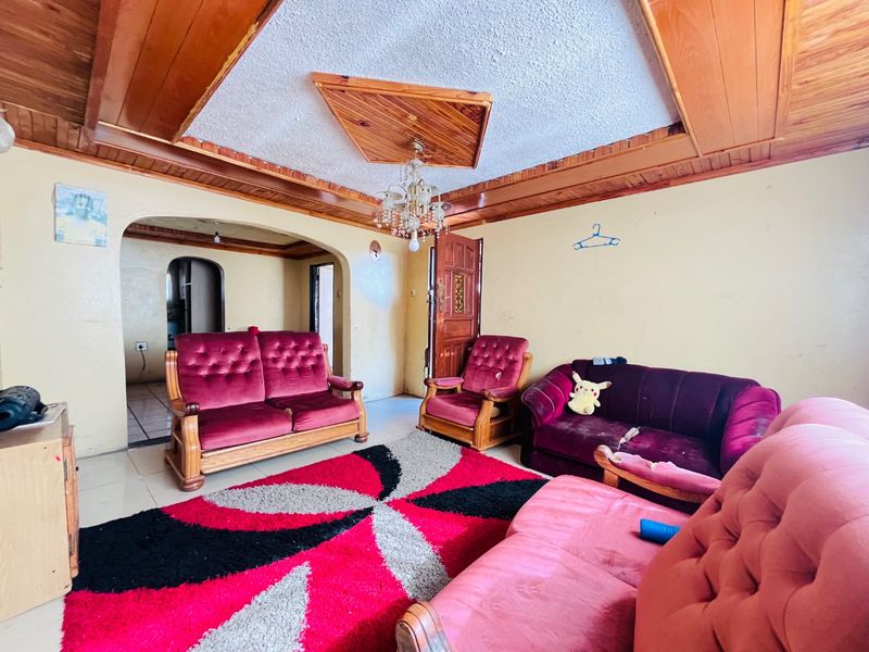 Spacious living room featuring a distinctive timber-clad ceiling with recessed detail, tiled flooring, and an arched entryway leading to adjacent living spaces.