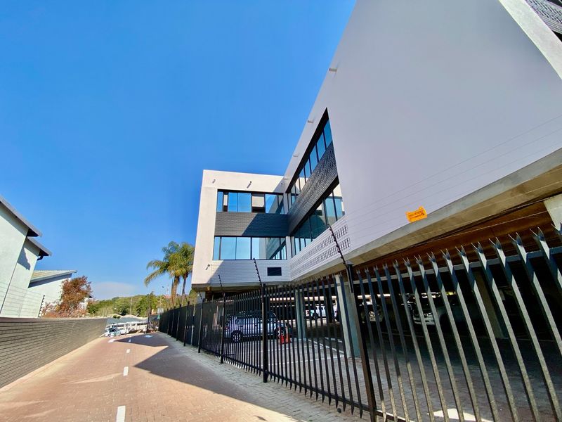 Modern commercial building exterior featuring a paved driveway, secure metal fencing with electric security, and a covered parking area.