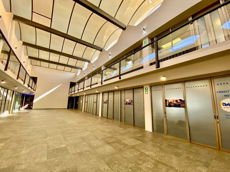 Spacious commercial atrium featuring a large curved skylight, mezzanine level with glass balustrades, and multiple glass-partitioned office units with tiled flooring.