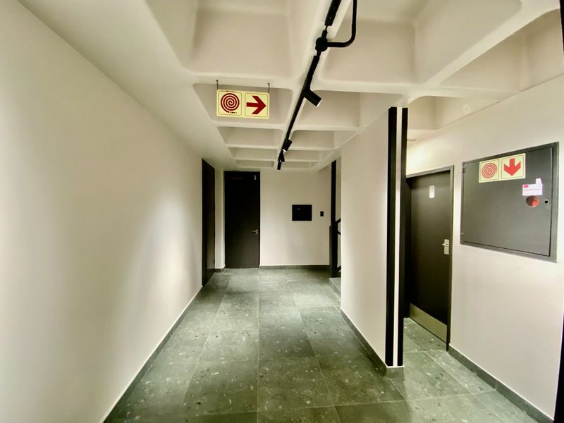 A modern commercial hallway featuring a distinctive waffle slab ceiling, track lighting, and durable tiled flooring with integrated fire safety infrastructure.