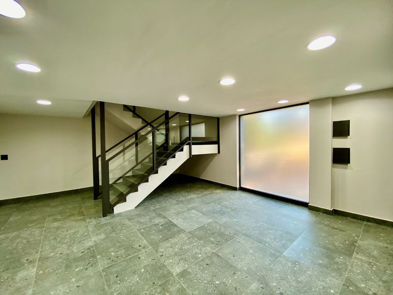 Modern commercial entrance lobby featuring large format floor tiles, a contemporary staircase with glass balustrade, and recessed ceiling lighting.