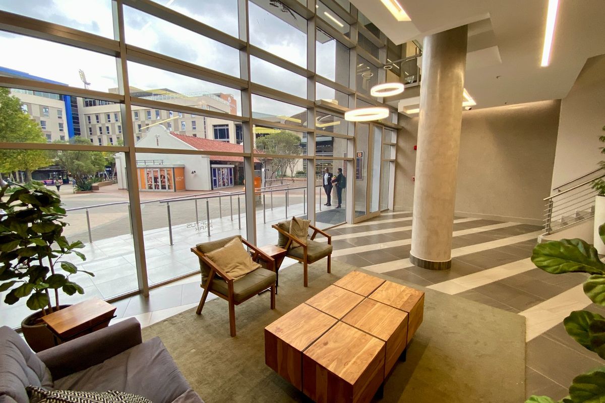 Modern commercial building entrance lobby featuring expansive floor-to-ceiling glass windows, high ceilings, structural columns, and contemporary tiled flooring.