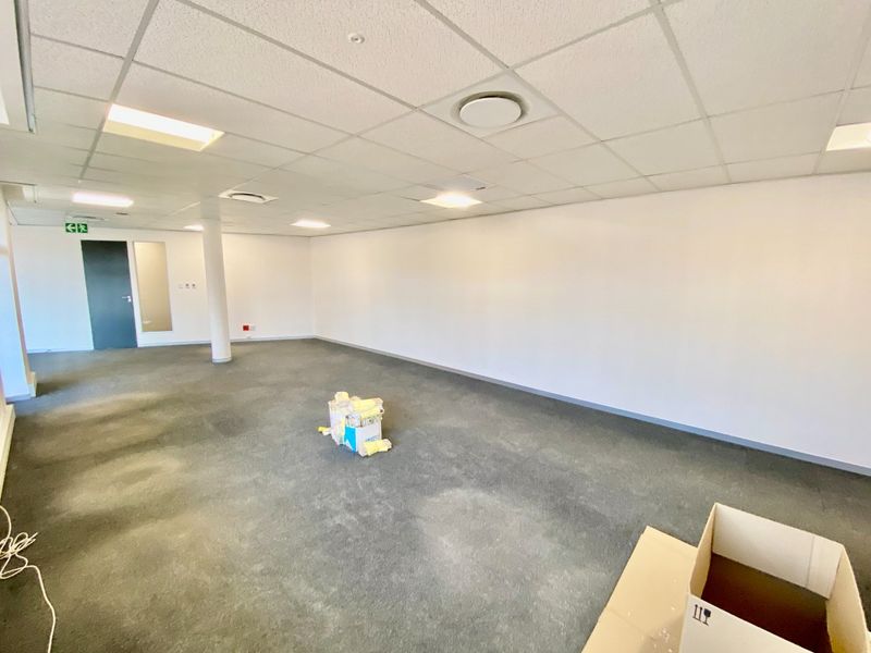 An open-plan commercial office space featuring a suspended ceiling, recessed lighting, and carpeted flooring, providing a versatile and functional workspace.