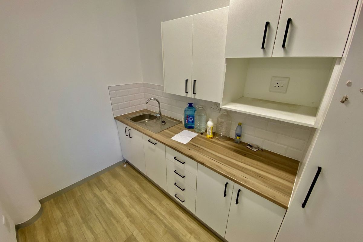 A clean, modern kitchenette featuring white cabinetry, wood-look laminate countertops, a stainless steel sink, and a subway tile backsplash.
