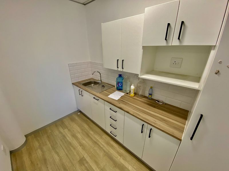 A clean, modern kitchenette featuring white cabinetry, wood-look laminate countertops, a stainless steel sink, and a subway tile backsplash.