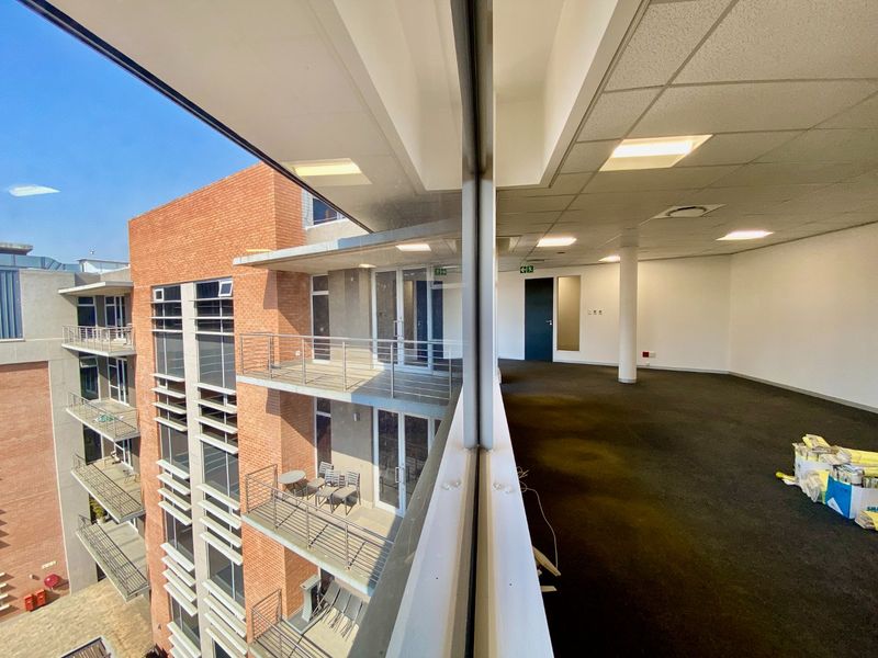 An empty commercial office space featuring carpeted flooring, recessed lighting, and large glass windows overlooking exterior balconies and the building facade.