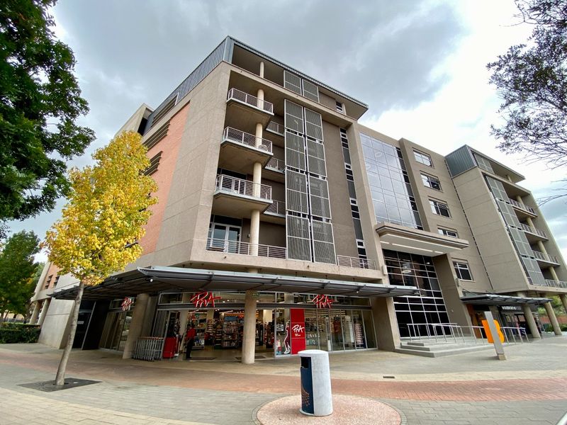 A modern multi-story commercial building featuring a glass facade, integrated balconies with metal railings, and a ground-level retail storefront.