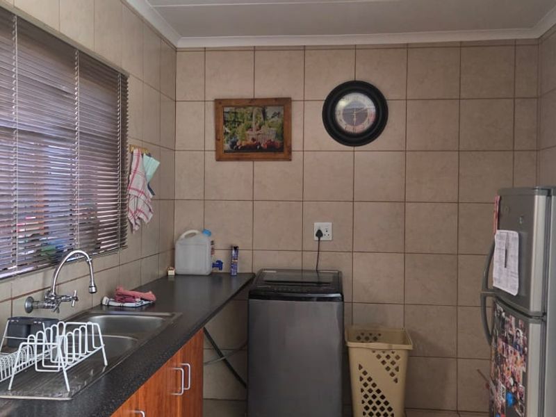 A functional laundry area featuring tiled walls, a stainless steel sink with mixer tap, and laminate countertop space for appliances.