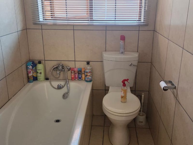 A functional bathroom featuring a bathtub, toilet, and neutral wall tiling, providing a clean and practical space.