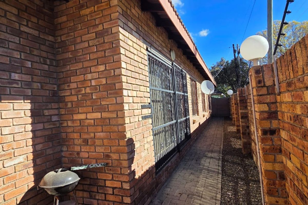 A side exterior view of the townhouse featuring face brick walls, a paved walkway, and secure perimeter fencing with integrated security features.