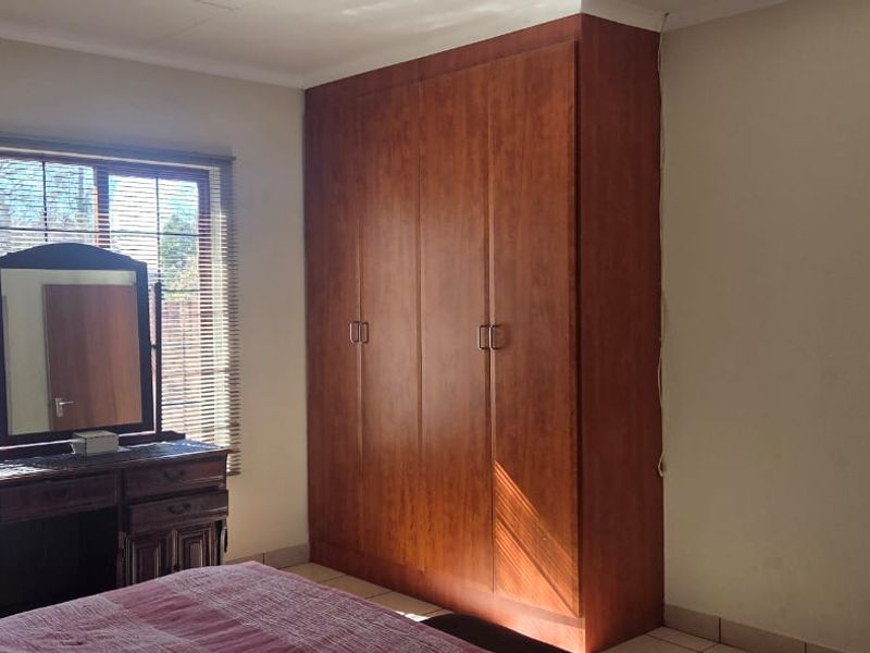 A bedroom featuring tiled flooring, a large built-in wooden wardrobe, and a window fitted with venetian blinds.