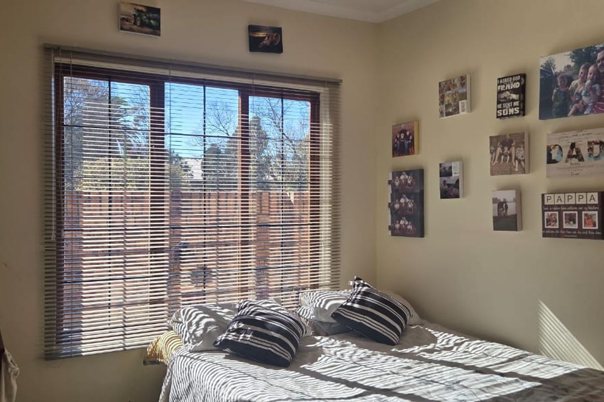 A bedroom featuring a large sliding window with venetian blinds, providing natural light and a view of the exterior.