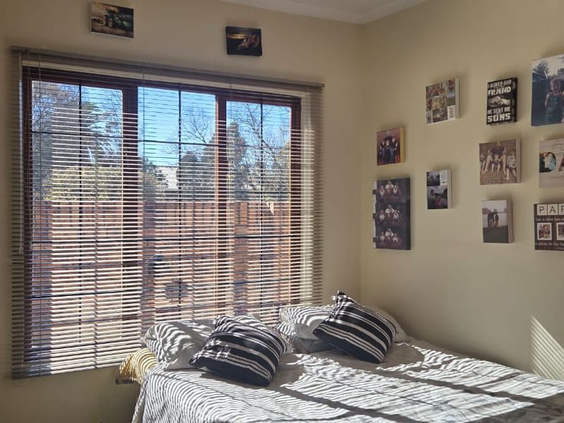 A bedroom featuring a large sliding window with venetian blinds, providing natural light and a view of the exterior.