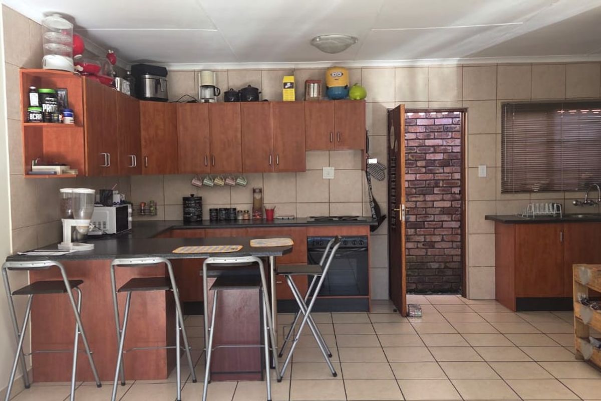 Functional kitchen featuring wood-finish cabinetry, tiled backsplash, built-in oven and hob, and a breakfast bar area with tiled flooring throughout.
