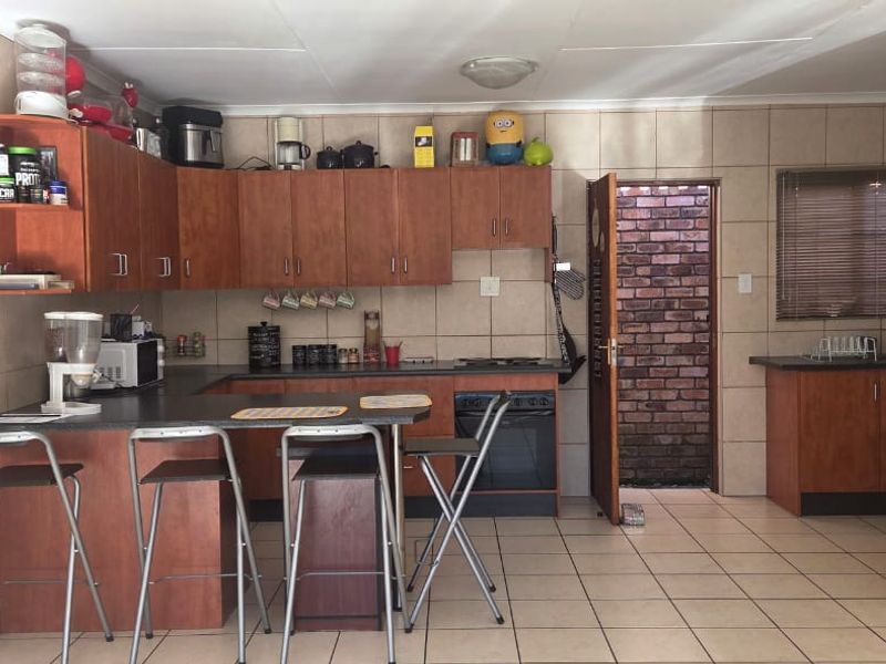 Functional kitchen featuring wood-finish cabinetry, tiled backsplash, built-in oven and hob, and a breakfast bar area with tiled flooring throughout.
