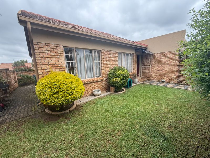 A well-maintained rear exterior view of a face brick townhouse featuring a private garden, paved walkway, and secure entrance.
