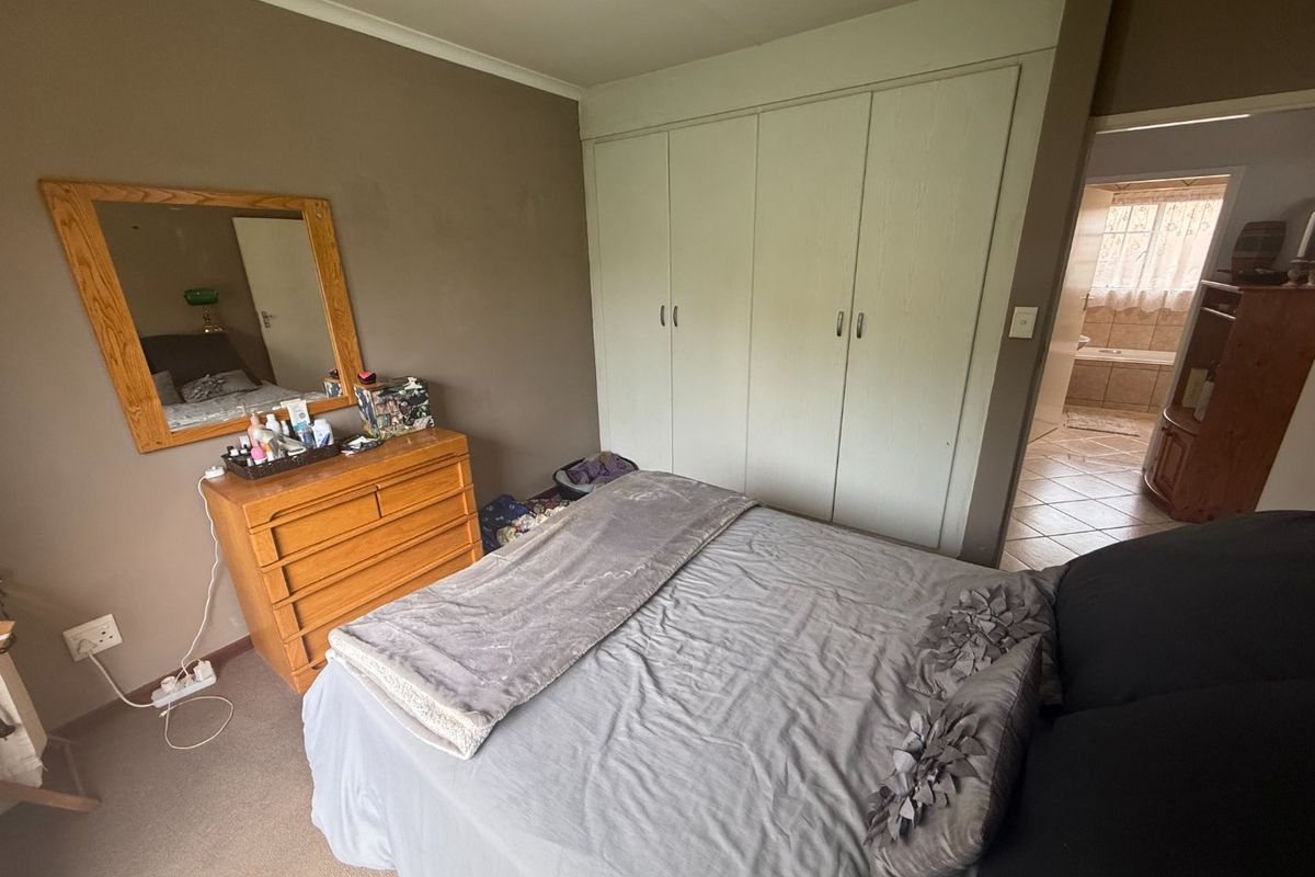 A bedroom featuring built-in cupboards and carpeted flooring, with an adjoining bathroom visible through the doorway.