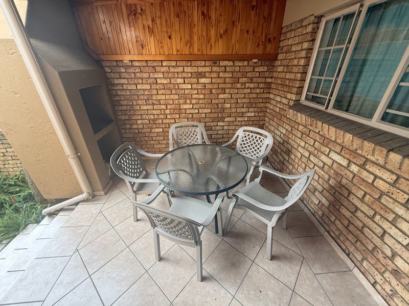 A covered patio area featuring exposed brick walls, a built-in braai, tiled flooring, and timber ceiling accents, providing a functional outdoor entertainment space.