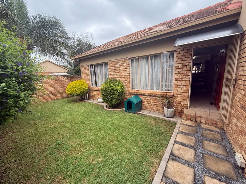 Rear view of a face brick townhouse featuring a small private garden, paved walkway, and secure entrance door.