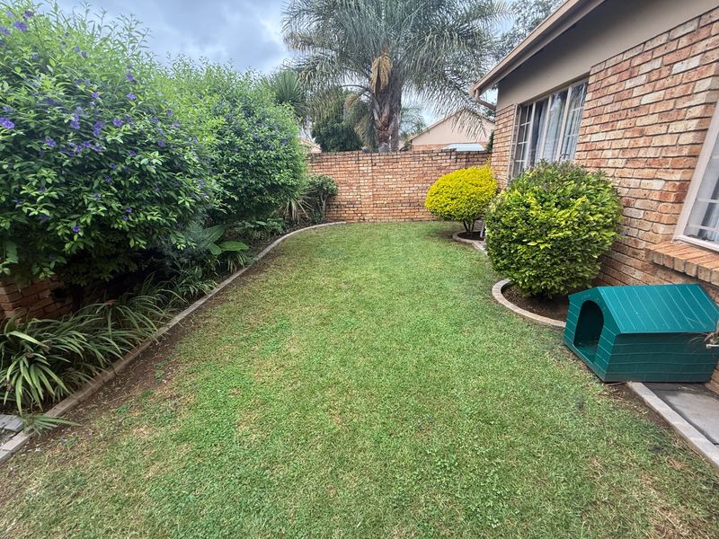 A well-maintained rear garden featuring a lush lawn, established shrubbery, and a solid brick boundary wall adjacent to the townhouse exterior.