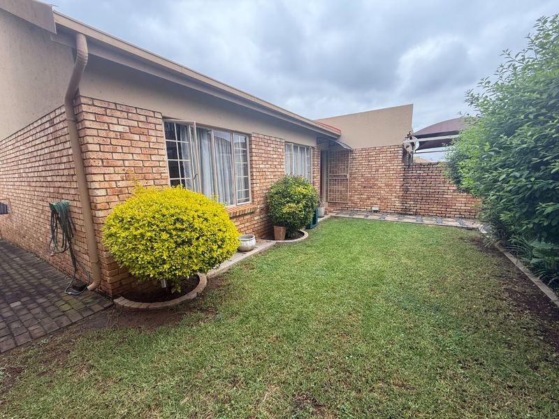 A private rear garden featuring a well-maintained lawn, face brick exterior walls, and a paved walkway leading to the townhouse entrance.