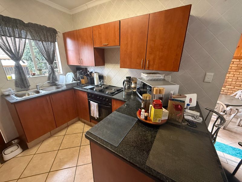 A functional kitchen featuring wooden cabinetry, granite countertops, a built-in oven and hob, and tiled flooring with a neutral backsplash.