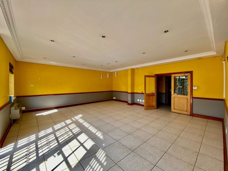 A spacious, empty commercial office area featuring tiled flooring, recessed lighting, crown molding, and a wall-mounted air conditioning unit.