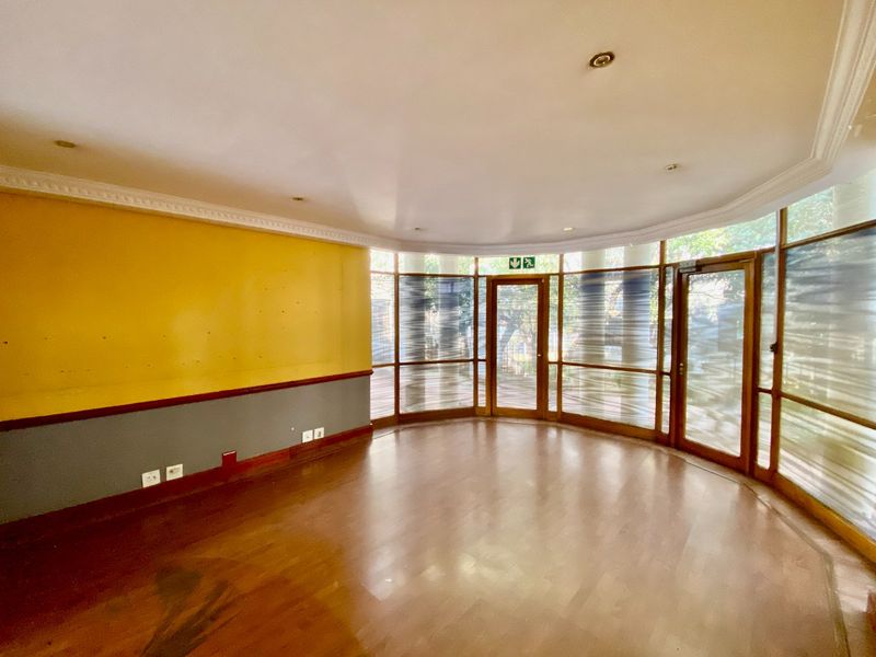 An empty, curved office space featuring laminate flooring, crown molding, and extensive glass windows providing natural light and exterior views.