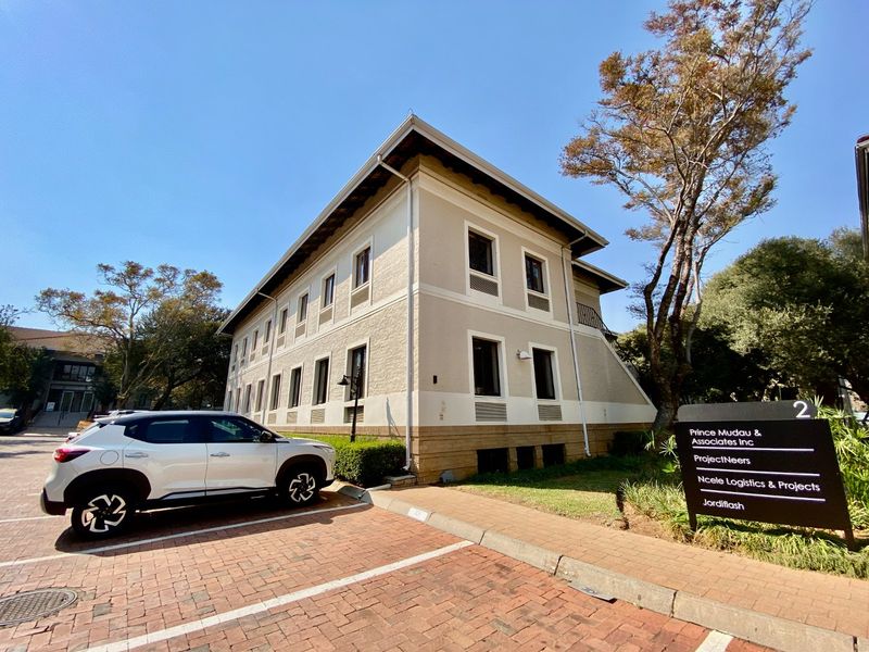 A well-maintained two-story commercial office building featuring a brick-paved parking area and professional signage at the entrance.