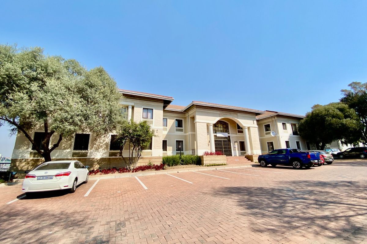 Front elevation of a commercial office building featuring a paved parking area, arched entrance with columns, and well-maintained exterior facade.