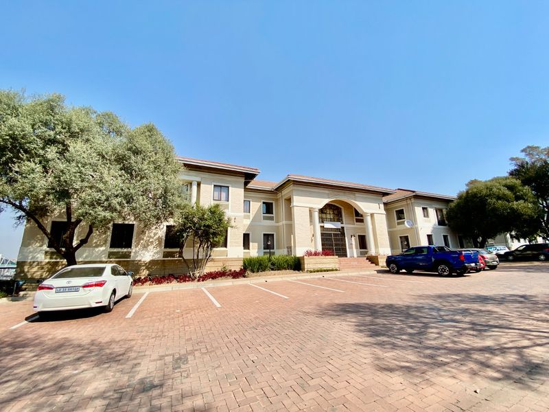 Front elevation of a commercial office building featuring a paved parking area, arched entrance with columns, and well-maintained exterior facade.