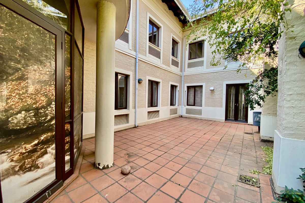 A spacious rear courtyard featuring terracotta tiling, structural columns, and multiple access points to the building interior.