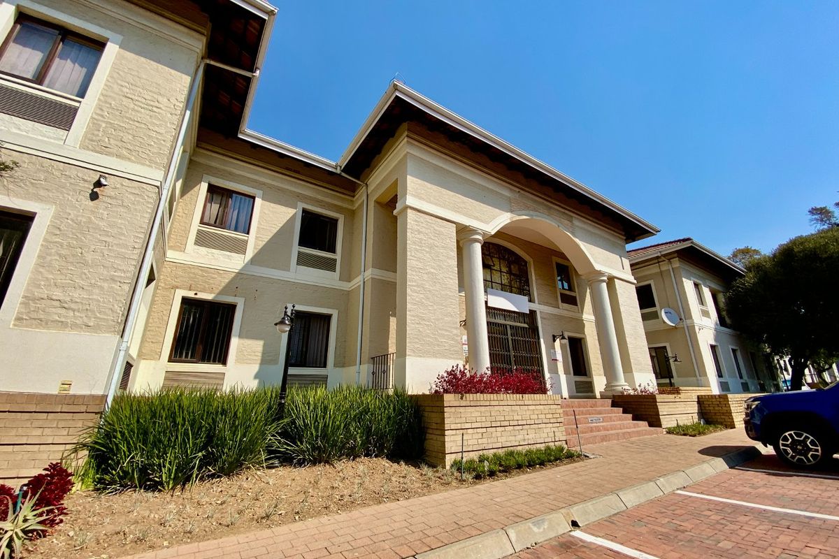 A well-maintained commercial building facade featuring classic architectural columns, an arched entrance, and paved parking area with established garden beds.