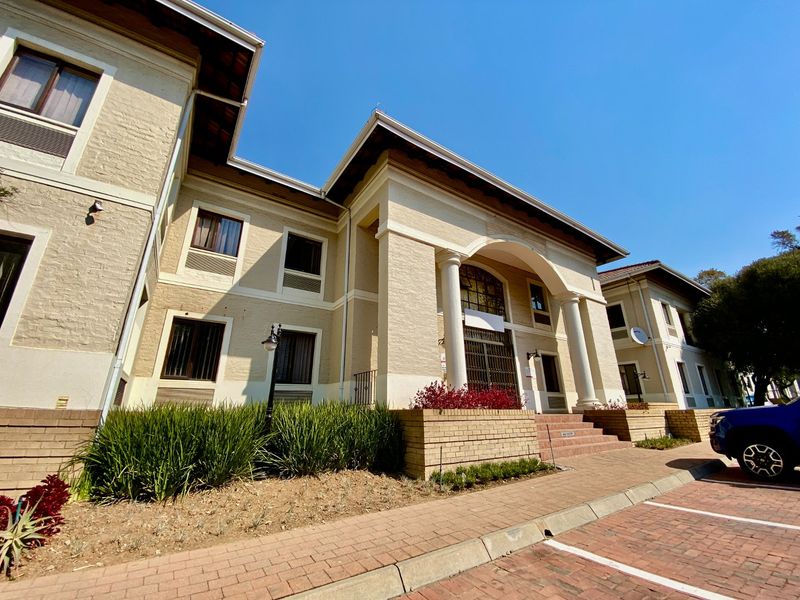 A well-maintained commercial building facade featuring classic architectural columns, an arched entrance, and paved parking area with established garden beds.