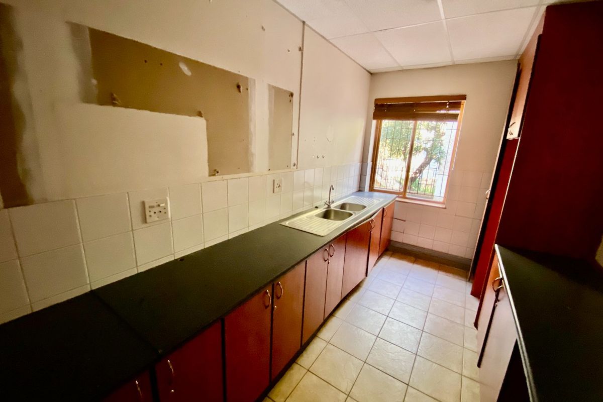 A functional kitchen space featuring laminate countertops, a double bowl sink, tiled splashbacks, and tiled flooring, currently requiring cosmetic updates and wall repairs.