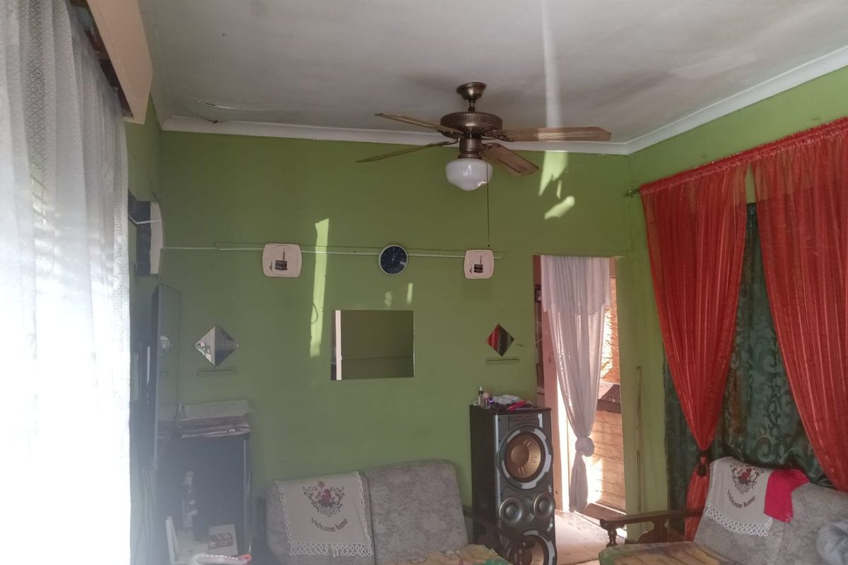 A living room featuring a ceiling fan and coving, currently showing signs of ceiling water damage and dated wall finishes.