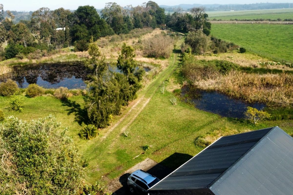 Aerial view of the farm property featuring natural ponds, expansive green fields, and a building with a corrugated metal roof.