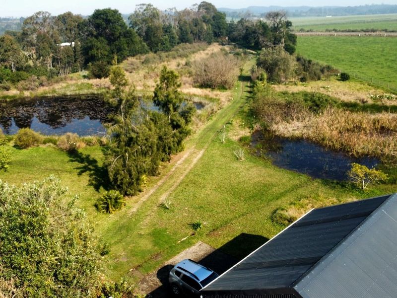 Aerial view of the farm property featuring natural ponds, expansive green fields, and a building with a corrugated metal roof.
