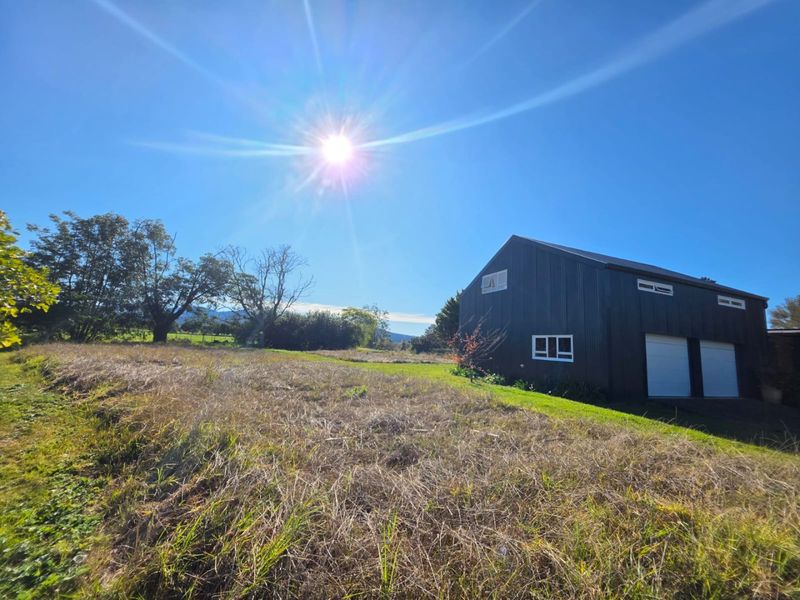 A view of the rear elevation of a dark-clad farm building featuring double garage doors and surrounding open pasture land.