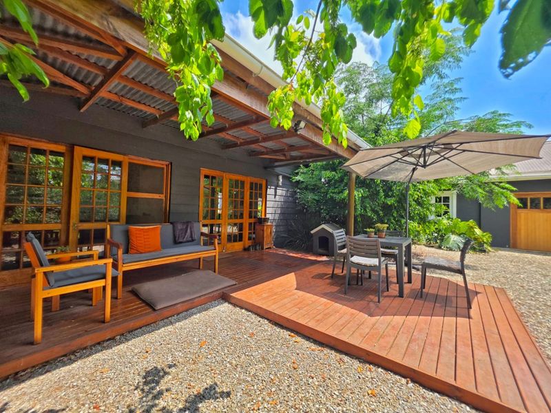 A well-maintained outdoor patio area featuring timber decking, a covered pergola with corrugated roofing, and direct access to the home through timber-framed glass doors.