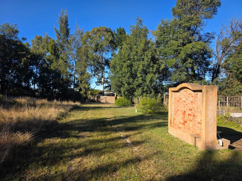 Expansive farm garden area featuring a decorative brick feature wall, mature trees, and perimeter fencing.