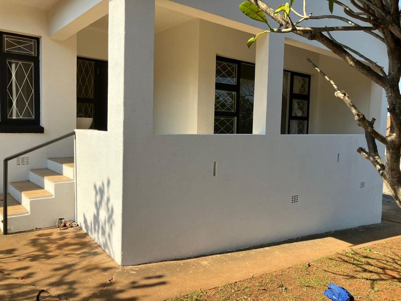 A covered outdoor patio area featuring concrete steps with a metal handrail and security-barred windows, providing a functional transition space to the home.