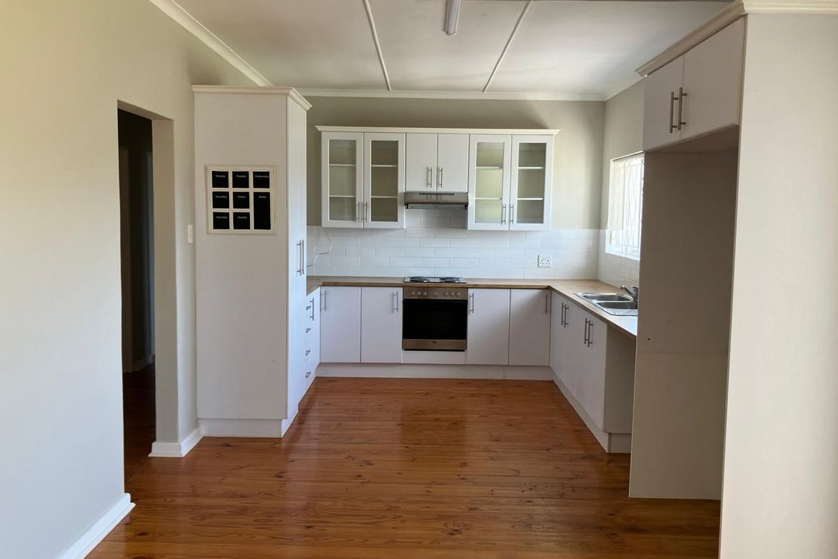 A clean, functional kitchen featuring white cabinetry, timber flooring, a built-in oven, extractor fan, and a tiled backsplash.