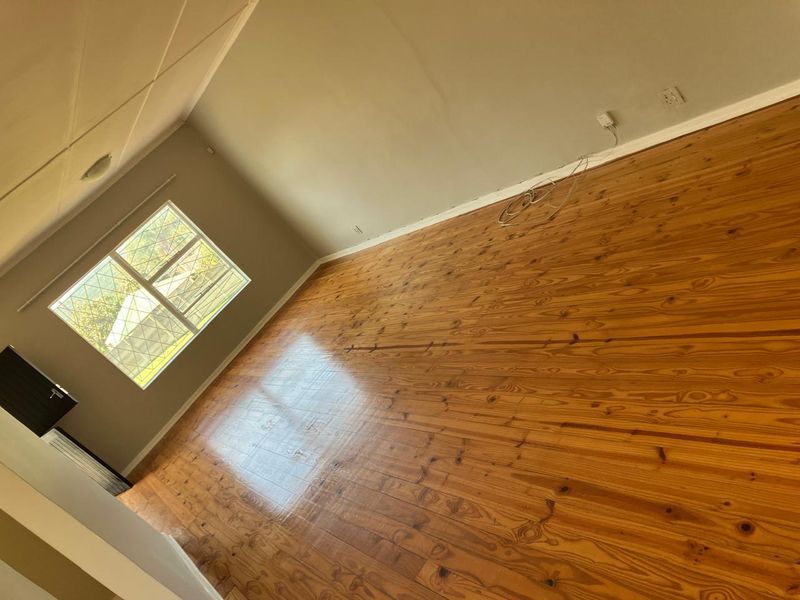 An empty living room featuring polished timber flooring, security bars on the window, and a neutral wall finish.