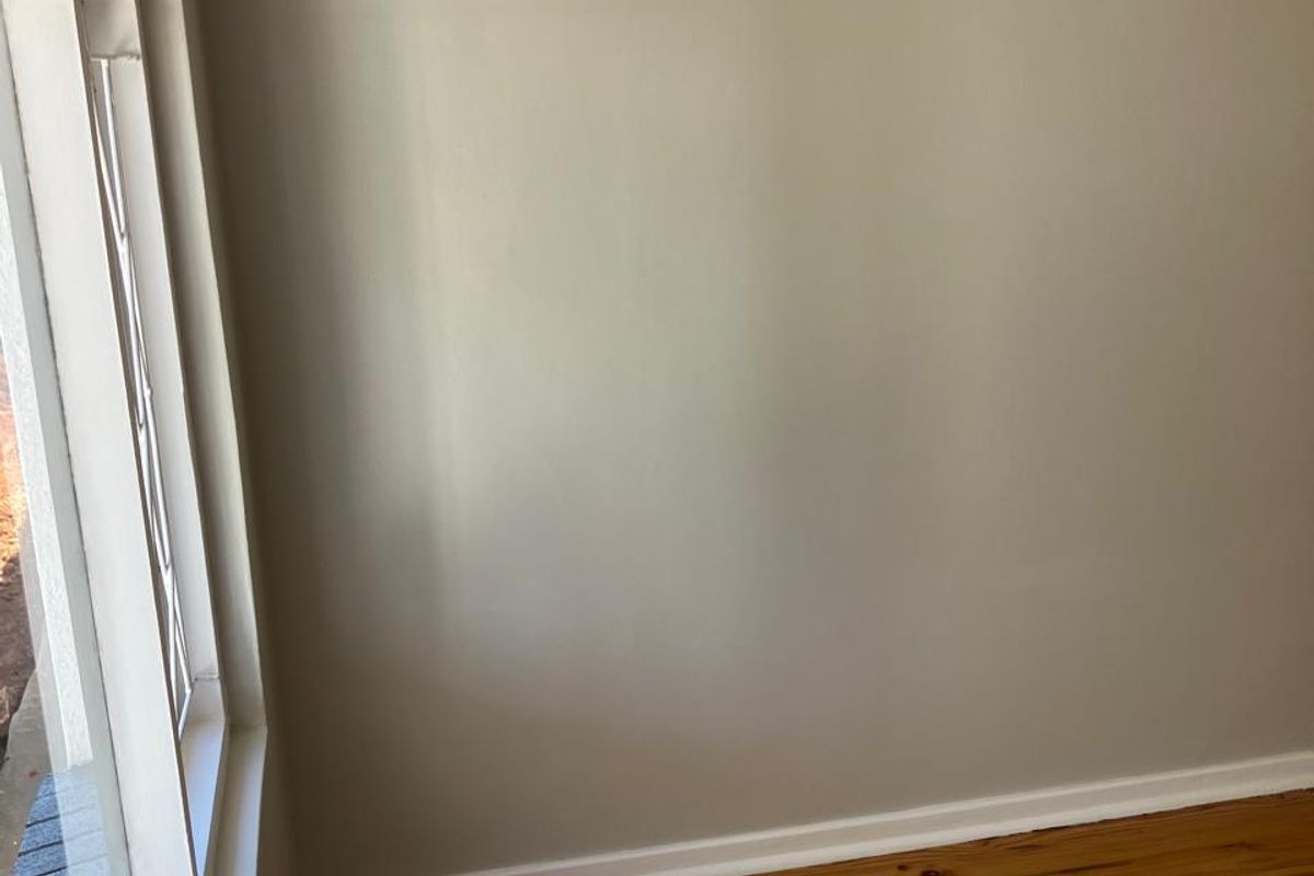 A bright, empty bedroom featuring polished timber flooring and a classic leaded glass window with neutral wall finishes.