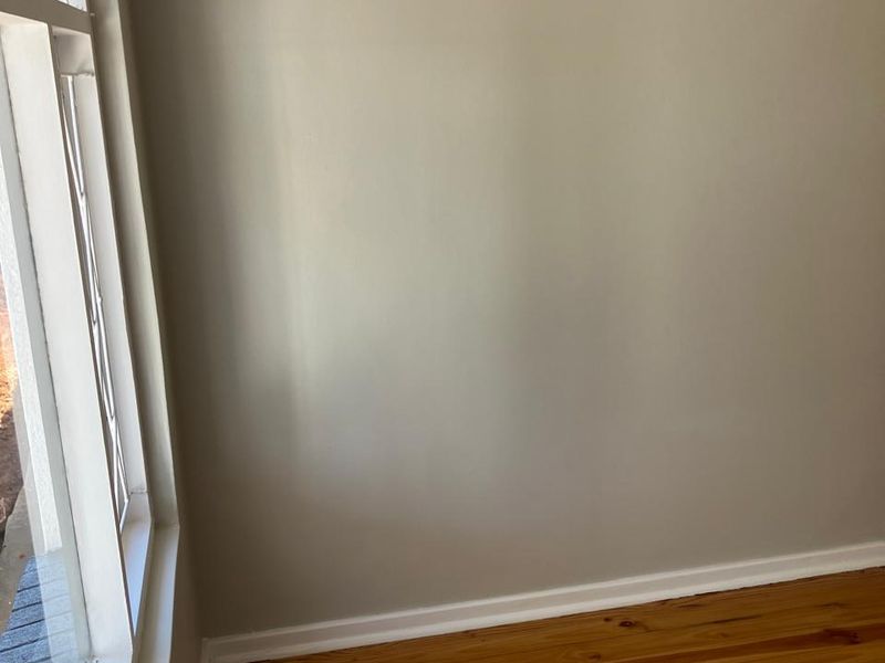 A bright, empty bedroom featuring polished timber flooring and a classic leaded glass window with neutral wall finishes.