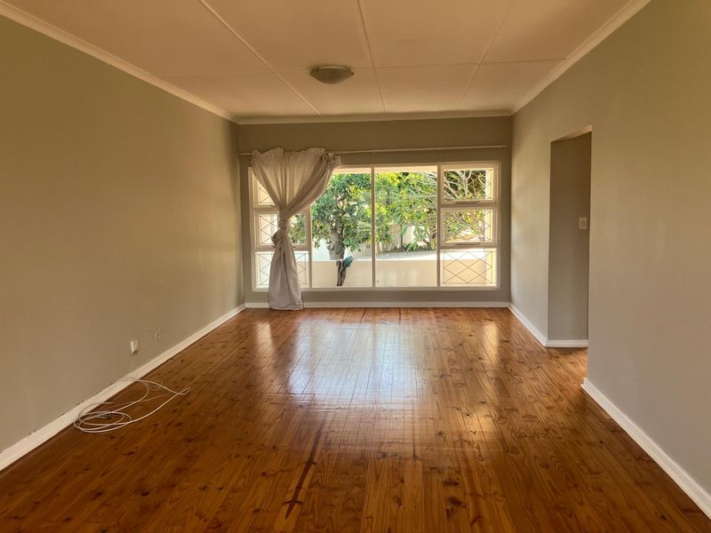 A spacious, empty living room featuring polished timber flooring and a large window with security bars, offering a bright and neutral canvas.