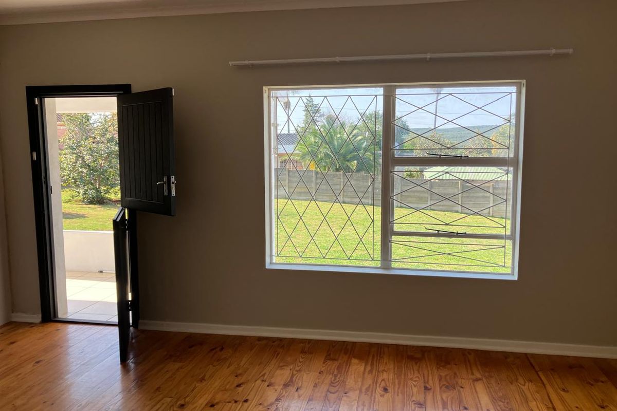 Bright living area featuring polished timber flooring, a stable-style door leading to the garden, and large windows with security bars.