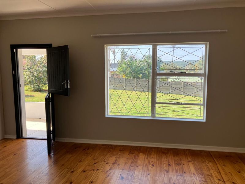 Bright living area featuring polished timber flooring, a stable-style door leading to the garden, and large windows with security bars.