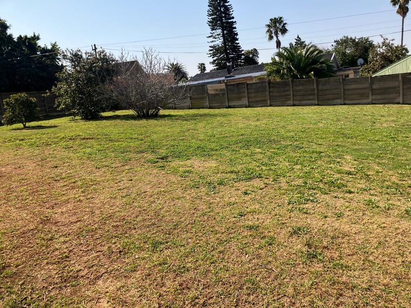 A spacious, open backyard area featuring a large lawn enclosed by a precast concrete boundary wall.